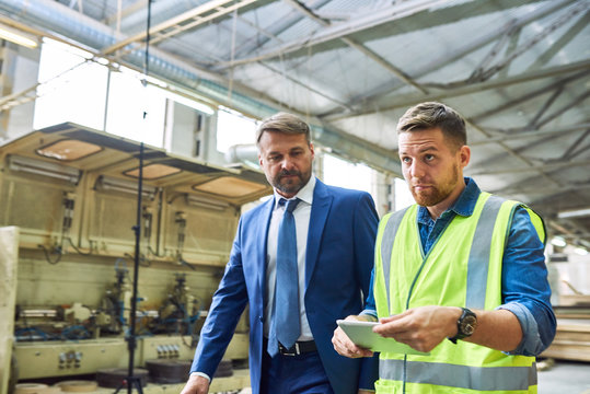 Portrait of workman giving tour of modern factory to handsome mature businessman discussing possible investment, copy space