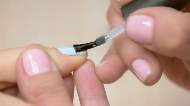 Manicurist fixing nail polish covering. Nail beautician doing manicure close up. Young woman receiving manicure in beauty studio.