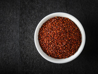 Quinoa in white bowl on blackwood. top view