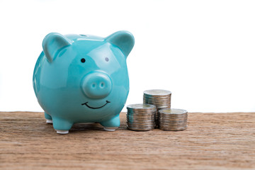 Saving money concept by green piggy bank and stack of coins on wood table with white background and copy space