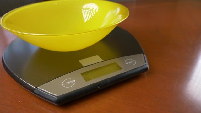 someone measures a piece of brown rice, on an electronic scale in the kitchen. pour the rump into a deep round bowl, standing on a flat weighing platform. 4k, slow motion, dolly shot