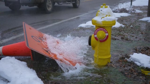 Yellow Fire hydrant spraying water out onto road in winter