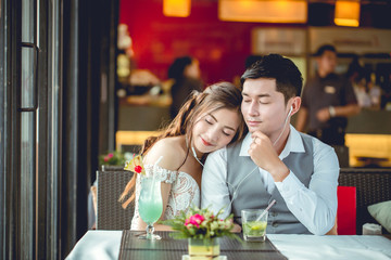 Asian girl and her boyfriend listen music by earphone in restaurant. They be sleepy.