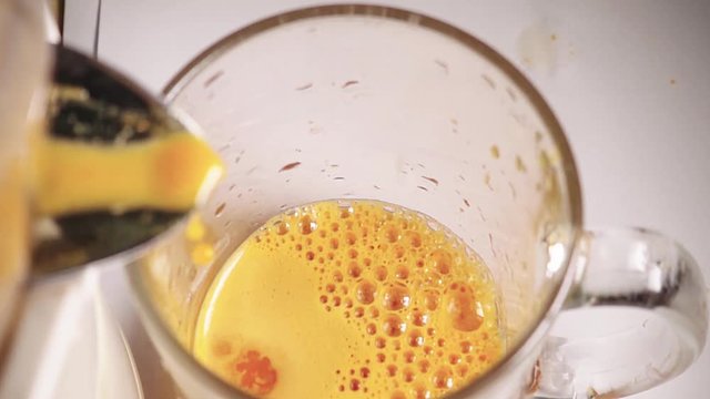Fresh squeezed carrot juice is poured into the cup, slow motion