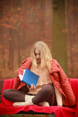 Obraz premium Blonde girl reading book in autumn scenery