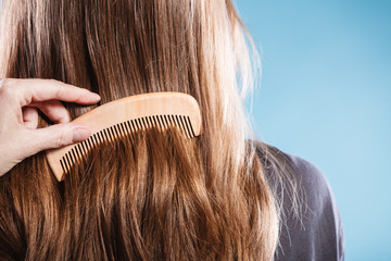 Female hand combing hair with wooden comb