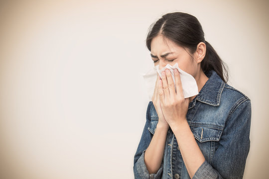 Woman with a cold blowing her runny nose with tissue. Portrait of Asian beautiful girl get sick sneezing from flu. Healthcare and medical concept.