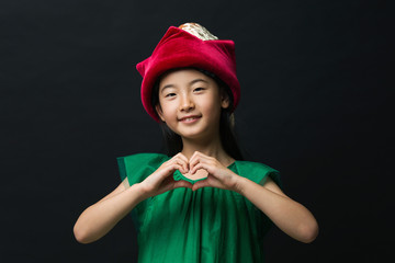 Cute Asian girl dressed in fairy hat and hand-made heart, green dress on black background.