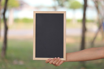 Hand of a business woman holding a empty black wooden picture frame on blur garden background.