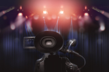rear of professional video camcorder with set of light hanging in television studio background.