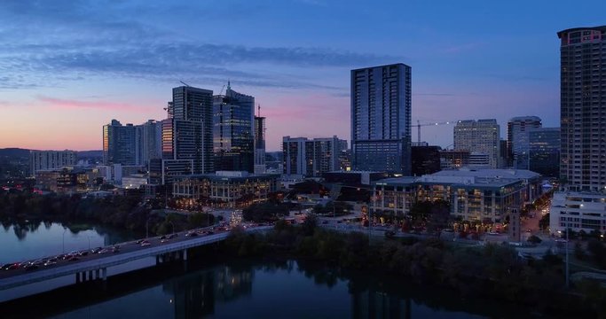 A slow lowering reverse aerial establishing shot of the Austin, Texas skyline on an early Winter evening as traffic passes over the South 1st Street Bridge.  	
