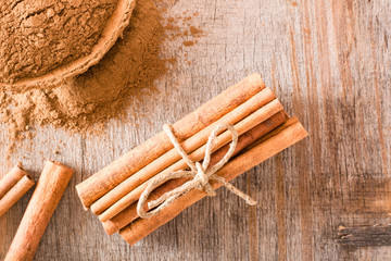 Cinnamon sticks, tied with a rope, and ground cinnamon in a bowl lie on a wooden table. Top view