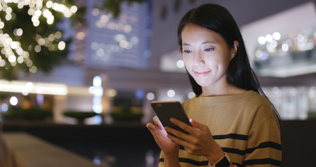 Woman looking at cellphone with Christmas decoration light of the background