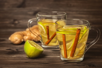 two cup of soothing tea with ginger, lime and cinnamon on wooden background, close up