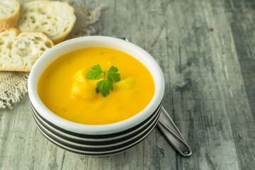A bowl of pumpkin potato vegetable soup with bread and garnish on a rustic wooden table background with copy space for your text