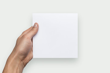 Mockup square empty blank white postcard holds the man in his hand. Isolated on a gray background