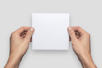 Obraz premium Mockup square empty blank white postcard holds the man in his hand. Isolated on a gray background