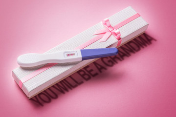 You will be a grandma. Positive pregnancy test with two strips and a gift box with a pink ribbon and bow. The girl is born