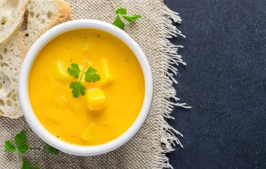 A bowl of pumpkin potato vegetable soup with bread and garnish on a dark background with copy space...
