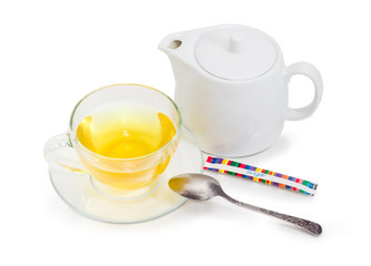 Green tea in glass cup on saucer, tea spoon, teapot