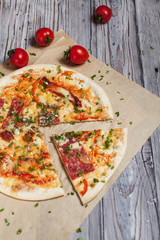 Pizza with a thin crust with cheese, bacon, pepper and herbs on a light wooden background