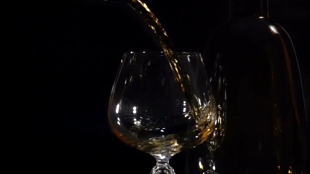 Cognac is poured into a glass in Slow Motion on a black background