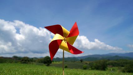 Paper windmill in the lawn with cloud and mountain background