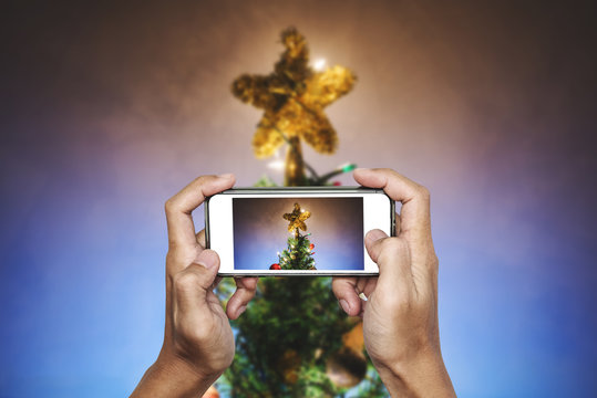Hands holding mobile smart phone, taking photo of Christmas star on Christmas tree with colorful lights