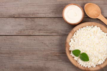 Cottage cheese in a wooden bowl with sour cream on old wooden background with copy space for your text. Top view