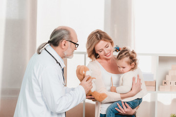 Obraz premium portrait of senior doctor, smiling mother with little girl on hands in clinic