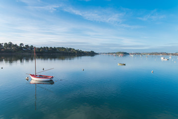 Rowboat, white and red boat and buoys in Brittany, on a glassy sea, with the Morbihan gulf in background 
