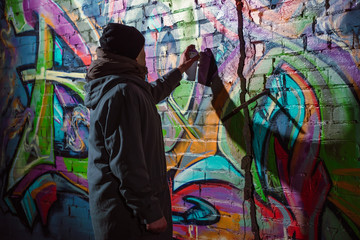 Fototapeta na wymiar street artist painting graffiti with aerosol paint on wall at night