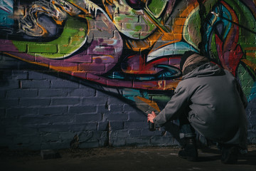 rear view of street artist painting graffiti with aerosol paint on wall at night