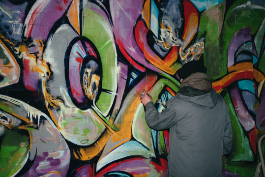 Back View Of Street Artist Painting Graffiti With Aerosol Paint On Wall At Night