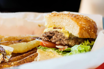 Junk food background: Half blue cheese burger with beef and vegetables on white paper with golden potato. Unhealthy meal concept. Text space
