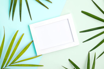 tropical mock up with white photo frame and palm leaves on colorful blue and green background. Travel concept. Trendy colors. Text space