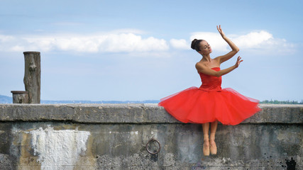 Portrait of a beautiful light ballerina, in a lush red dress, sits on a stone pier, tender....