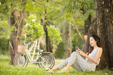 Asian woman lifestyle in park outdoor, using smart phone listen to music for relaxation and happy in summer