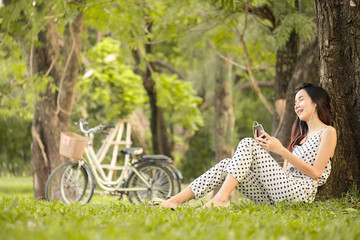 Fototapeta na wymiar Asian woman lifestyle in park outdoor, using smart phone listen to music for relaxation and happy in summer