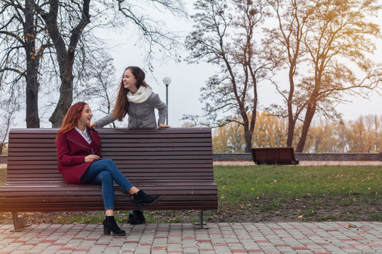 Female teenagers listening to music on smartphone at the bench in an autumn city park