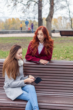Female teenagers listening to music on smartphone at the bench in an autumn city park