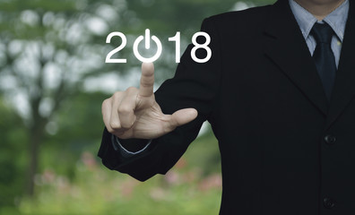 Businessman pressing 2018 start up business icon over blur flower and tree in park, Happy new year concept