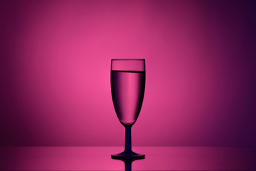 Wine in a glass goblet on a pink background with a gradient spot and stream of light on dark tones 