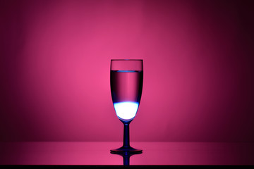 Wine in a glass goblet on a pink background with a gradient spot and stream of light on dark tones 