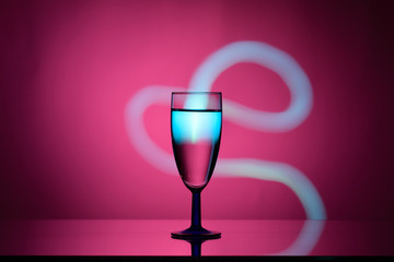 Wine in a glass goblet on a pink background with a gradient spot and stream of light on dark tones 