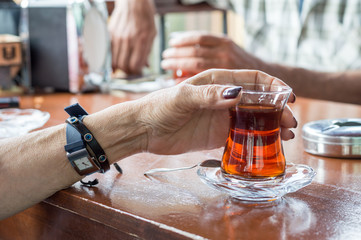 Close up of an old woman hand holding delicious red Turkish tea with traditional authentic glass on the table