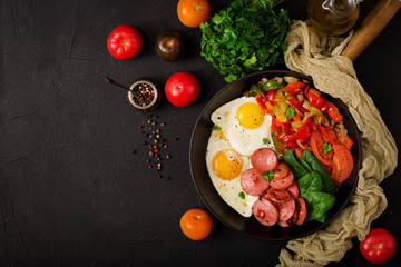 Déjeuner. Oeufs au plat avec saucisses et légumes dans une poêle à frire sur fond noir dans un style rustique. Vue de dessus