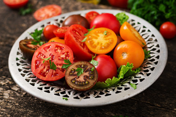 Tomatoes of different colors with green herbs in a bowl on a black background