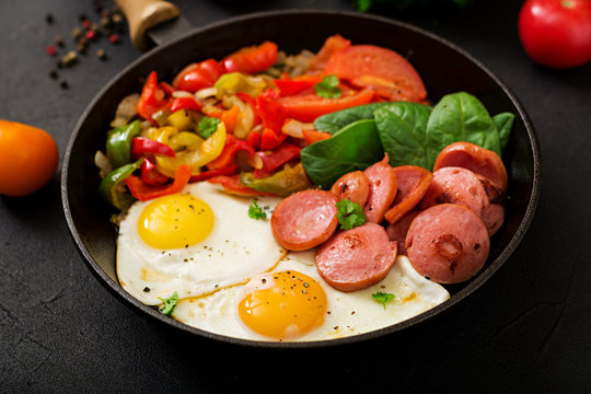 Breakfast. Fried eggs with sausage and vegetables in a frying pan on a black background in rustic style.