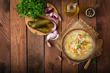 Soup with pickled cucumbers and pearl barley - rassolnik on a wooden background. Top view.
